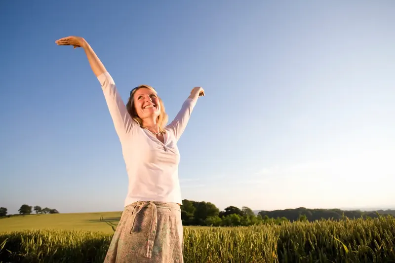 Smiling woman stretching out her arms in a wheat field